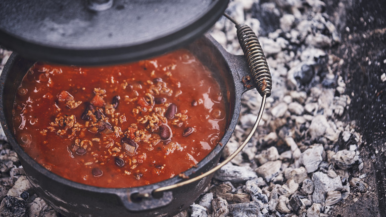 A bowl of chili cooking over a bed of coals