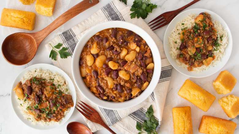 ground beef and mixed beans in a white bowl next to two white plates of ground beef and mixed beans over rice