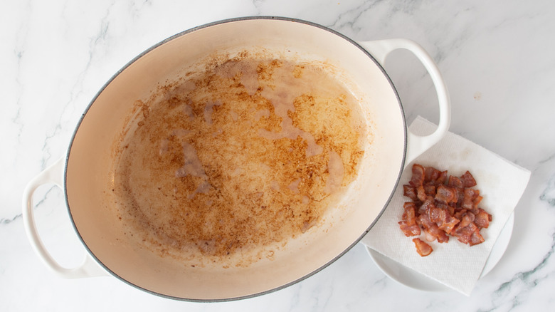 cooked bacon on a paper towel next to a white pot full of grease