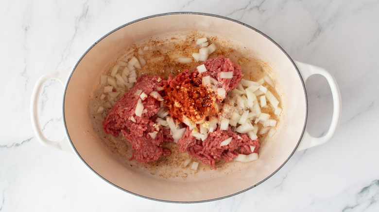 raw ground beef and chopped onions in a white pot