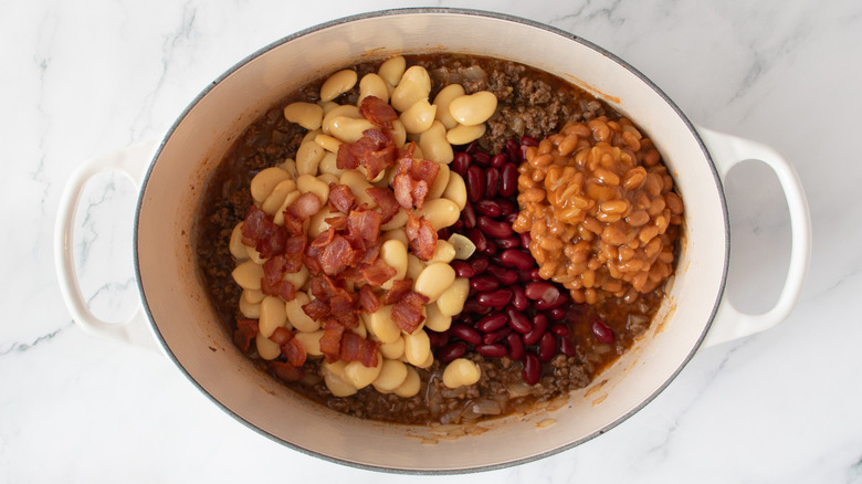 three types of cooked beans and cooked bacon bits in a white pot