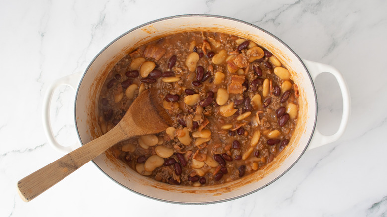 ground beef and mixed beans in a white pot with a wooden spoon
