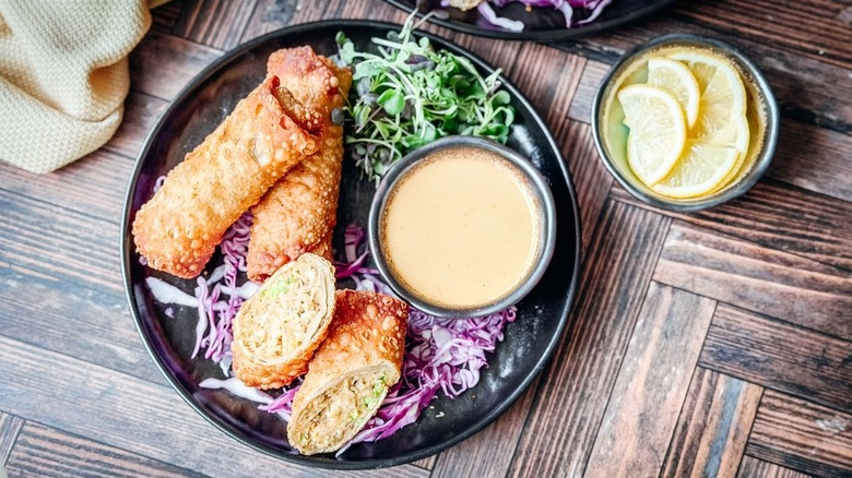 Whole and sliced crab cake egg rolls on serving plate with dipping sauce
