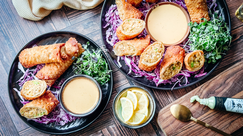 Crab cake egg rolls on serving platter and plate with shredded purple cabbage, micro greens, and dipping sauce