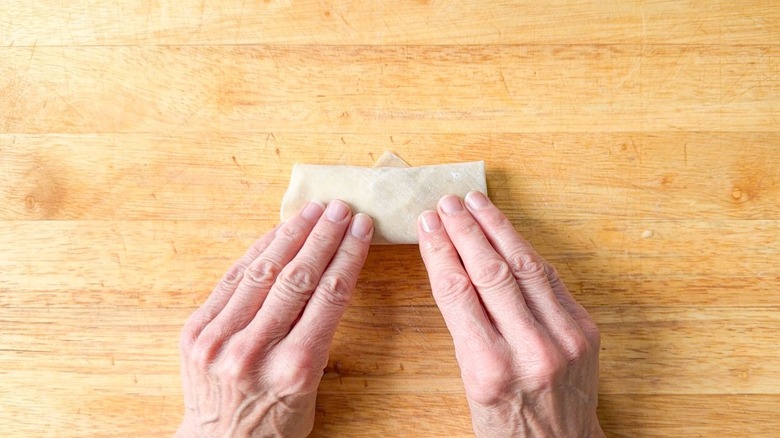 Rolling up a crab cake egg roll on a cutting board