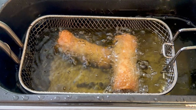 Crab cake egg rolls cooking in peanut oil in fryer