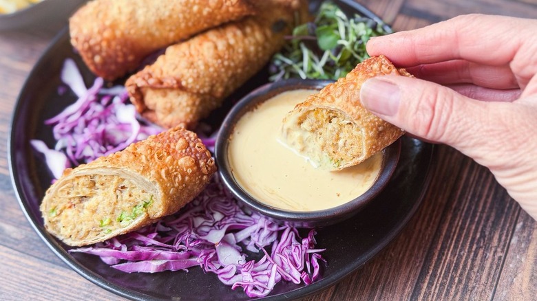 Dipping a crab cake egg roll half into lemon-soy aioli
