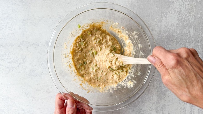 Mixing panko and scallions into crab cake egg roll filling in glass bowl
