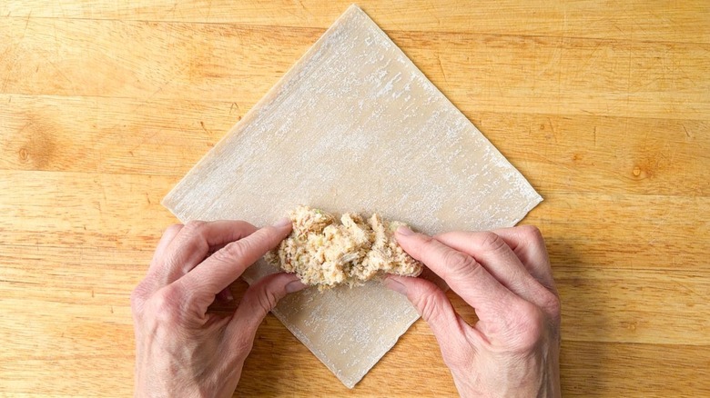 Adding crab cake filling to egg roll wrapper on cutting board