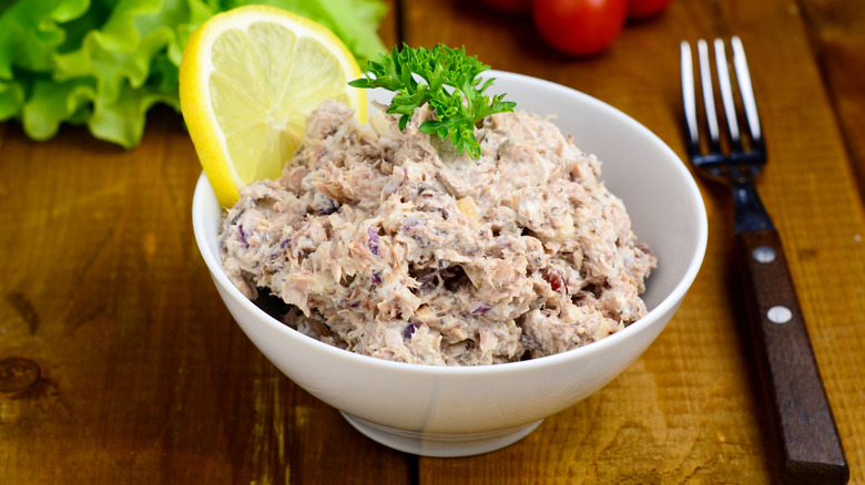A bowl of tuna salad with a lemon slice and parsley garnish