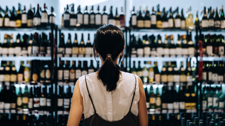A woman looking at a wall of wine bottles