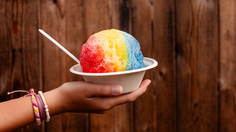 hand holds rainbow shaved ice in a white paper bowl