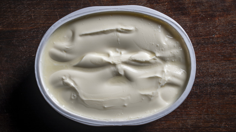 Overhead angle of an open tub of cream cheese on a dark wood surface