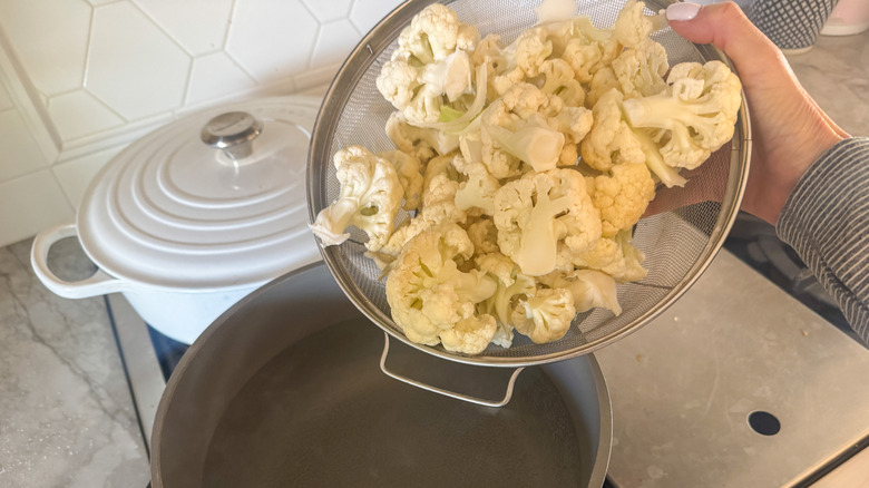 hand pouring cauliflower florets into pot