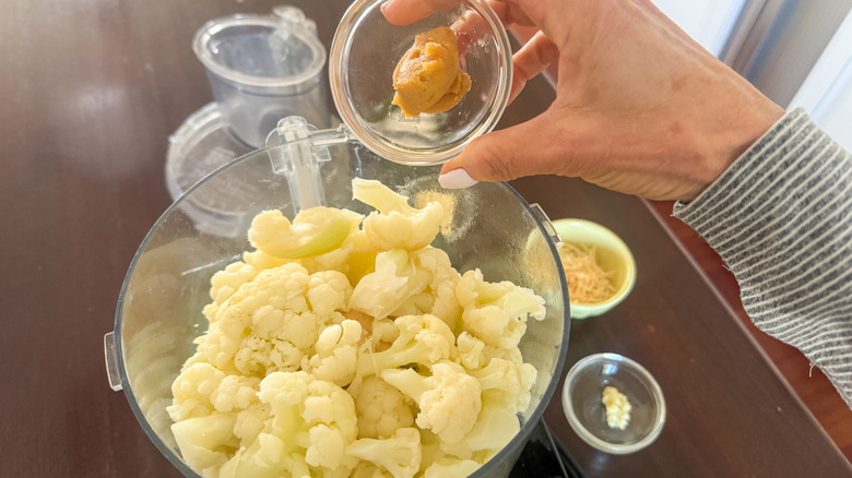 hand adding miso to processor with cauliflower florets