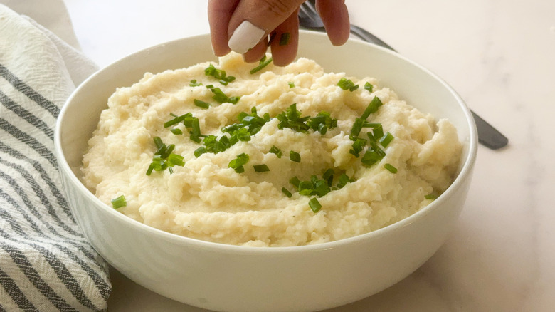 hand adding chives to cauliflower mash