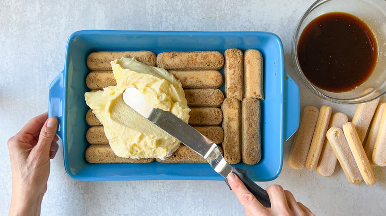 spatula spreading mascarpone over lady fingers 