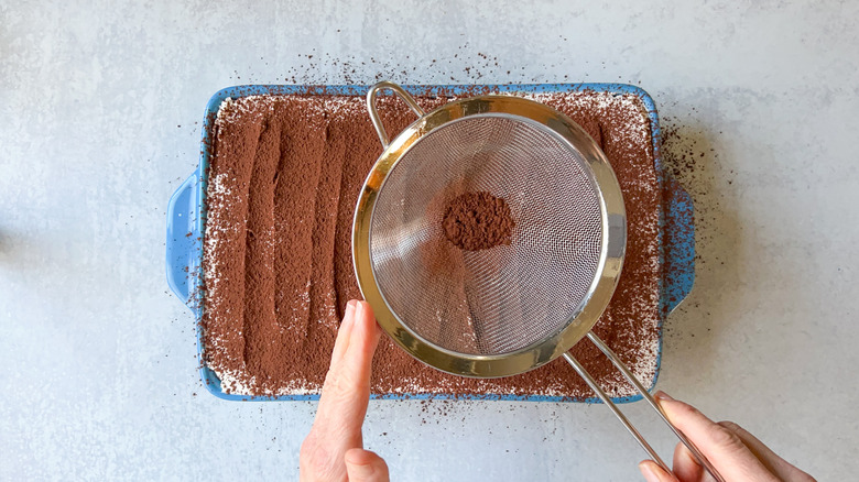 sifting cocoa powder over tiramisu