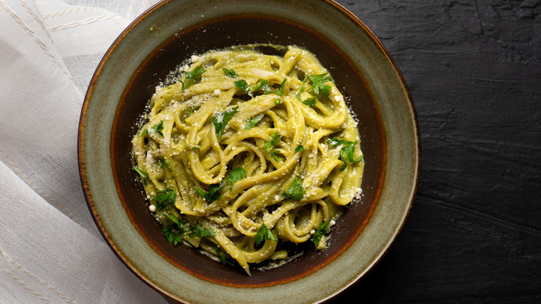 A plate of Mexican green spaghetti in brown and green dish on a  dark table