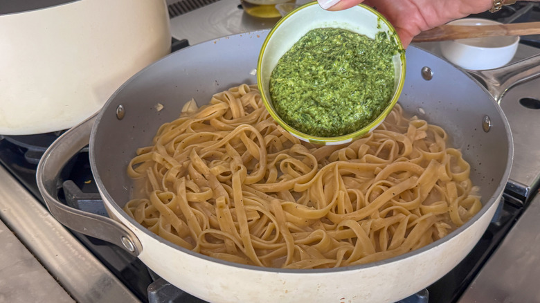 Bowl of pesto going into fettuccine pasta in pan
