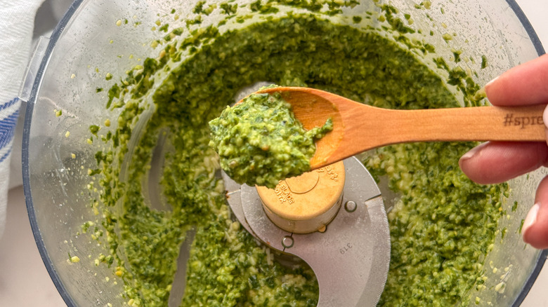 Spoon of pesto above pesto in food processor