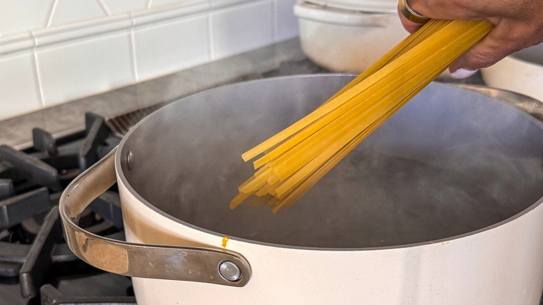hand adding fettuccine to pot