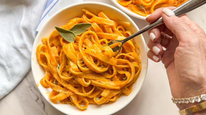 Hand swirling fork in pumpkin pasta