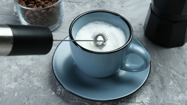 A milk frother whipping milk in a blue cup