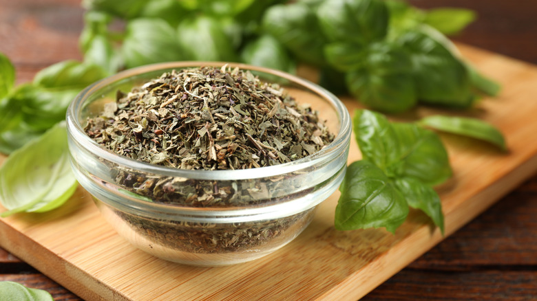 Dried basil leaves in a dish on a cutting board