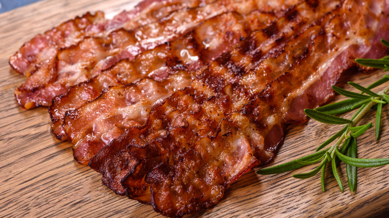 Slices of bacon on a cutting board with a sprig of rosemary