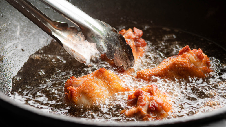 Frying oil in a pan with tongs