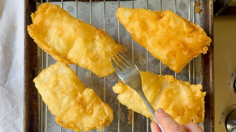Crispy beer-battered fish filets on rack over pan with fork