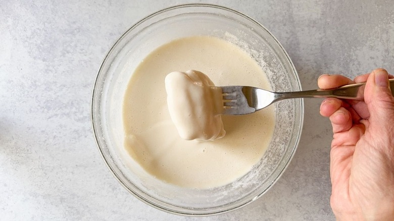 Dipping fish in beer batter in glass bowl with fork