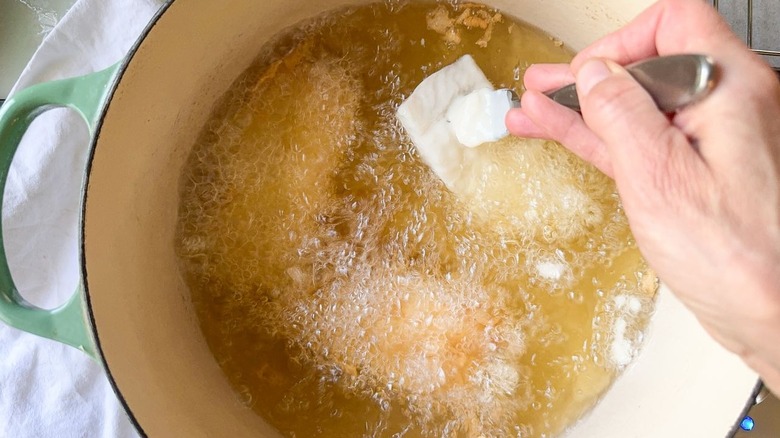Lowering battered fish into hot oil in pot on stove