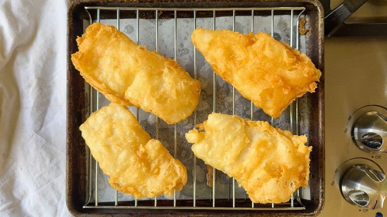Beer-battered fish filets on rack over parchment-lined baking sheet on stove