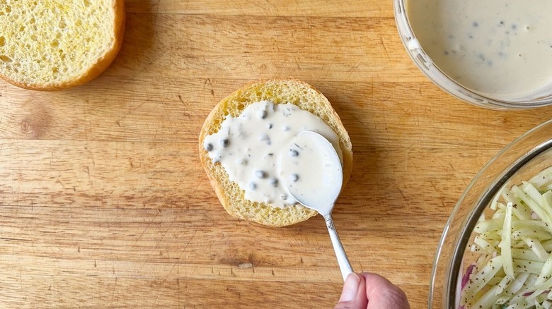 Spreading tartar sauce on toasted brioche bun with spoon