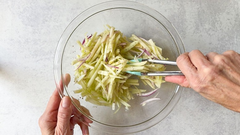 Mixing fennel slaw in glass bowl with tongs