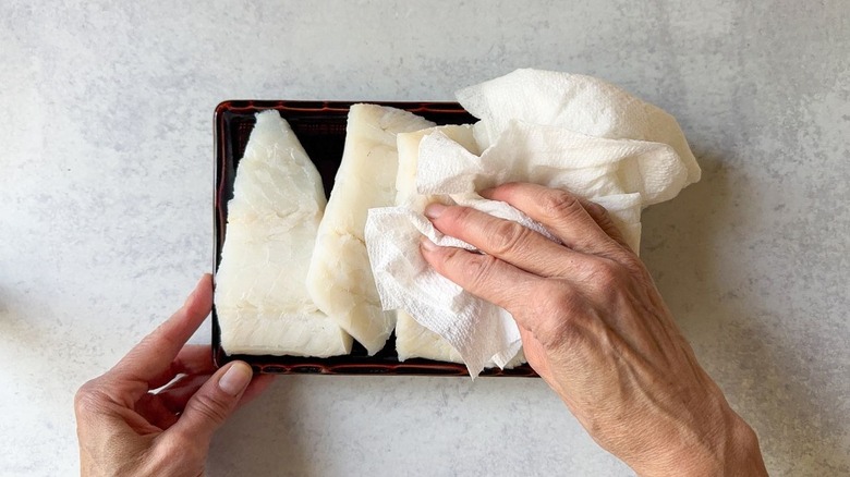 Patting dry cod filets with paper towel on brown plate