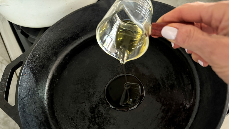 hand adding oil to skillet