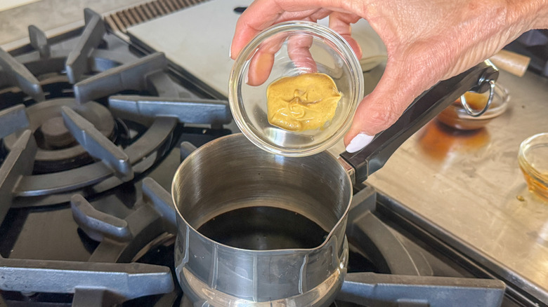hand adding mustard to pot