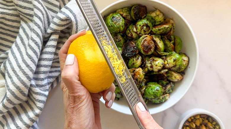 hand zesting lemon over bowl