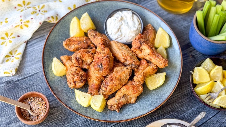 Crispy lemon pepper chicken wings on platter with lemon wedges and creamy feta dipping sauce