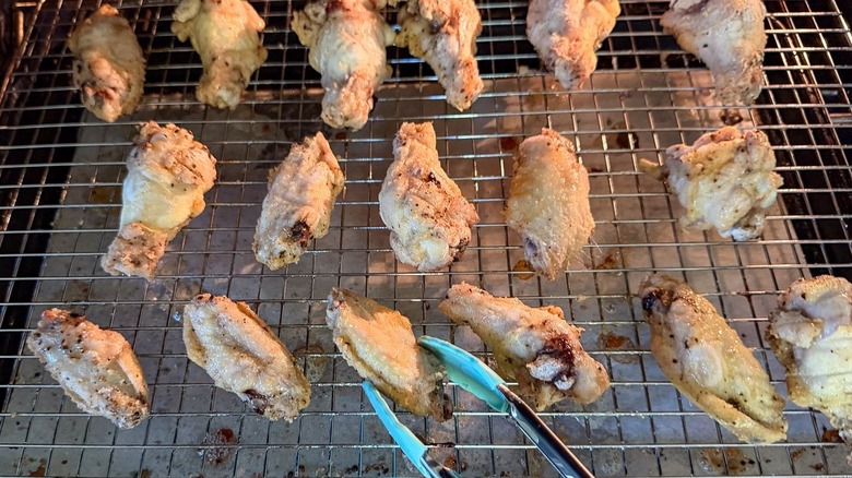 Flipping chicken wings on rack over baking sheet with tongs in oven