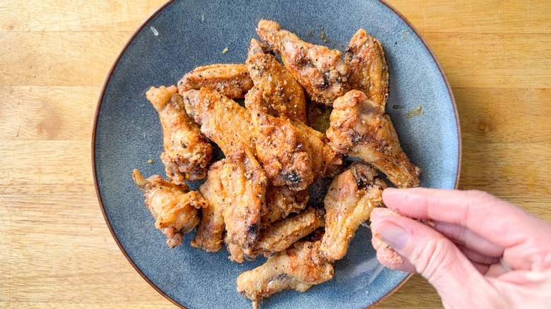 Sprinkling lemon pepper seasoning on baked chicken wings in serving dish