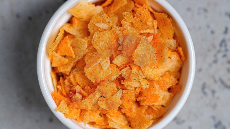 Top-down view of broken barbecue-flavored potato chips in a white bowl.