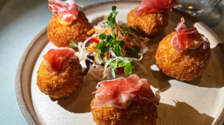 A plate of croquettes garnished with pieces of thin sliced meat