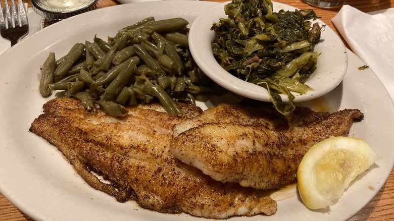 Grilled catfish entree from Cracker Barrel served on a white plate with green beans, turnip greens, and a lemon slice
