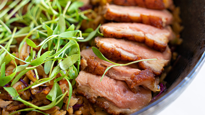 A bowl of fried rice topped with slices of seared duck and micro greens