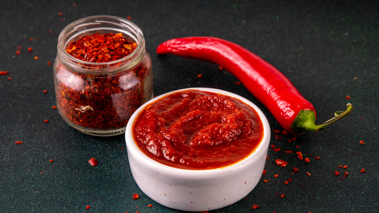 A jar of gochujang with Korean chili flake and a red pepper next to it