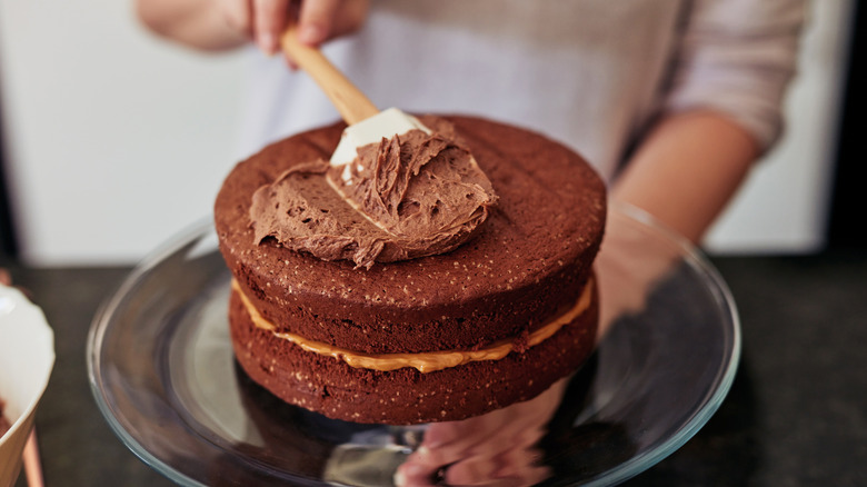 Person frosting a chocolate cake